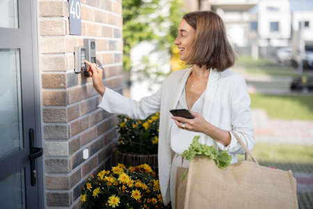 Young business woman going home with groceries, enters a password on the keyboard to access. Concept of modern technologies in everyday lifeの写真素材