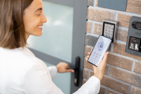Woman puts the smart phone to the electronic reader to access the apartment or office. Cell with...