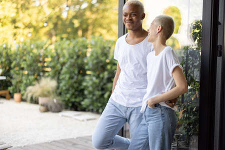 Multiracial couple standing and resting together on home terrace. Concept of relationship. Modern domestic lifestyle. Black man and european girl enjoying time together. Sunny daytimeの写真素材