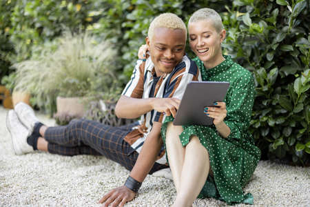Multiracial couple watching something on digital tablet at home garden. European girl and black man spending time together. Concept of leisure and relationship. Modern domestic lifestyleの写真素材