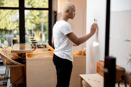 Black man choosing temperature on . Young focused guy pushing button on smart home system. Concept of modern domestic lifestyle. Interior of kitchen in modern apartment.の写真素材