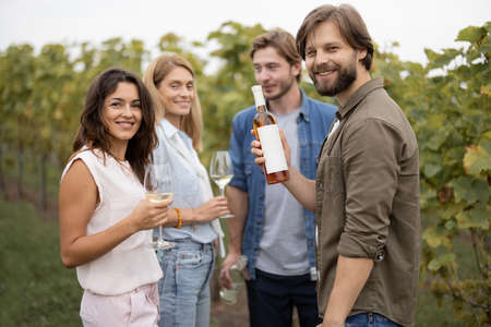 Joyful european friends tasting local wine near vineyards in countryside. Concept of winemaking. Young men and women enjoying time together. Idea of friendship and leisure. Green tourismの写真素材