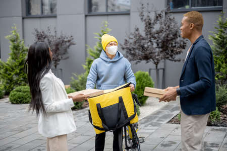 Businesspeople taking order from courier in medical mask and with bicycle. Concept of shipping and logistics during Coronavirus pandemic. Idea of break on job. Smiling men and womanの写真素材