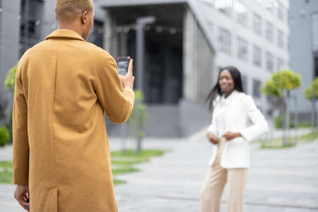 Man taking photo on smartphone of his girlfriend on city street. Concept of relationship. Idea of modern technology. Couple wearing fashion clothesの写真素材