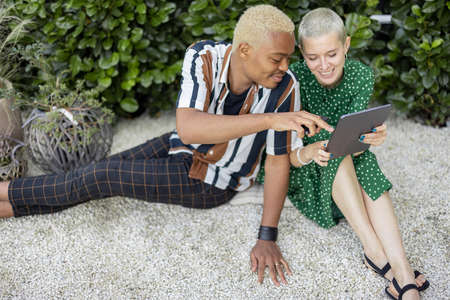 Multiracial couple watching something on digital tablet at home garden. European girl and black man spending time together. Concept of leisure and relationship. Modern domestic lifestyleの写真素材