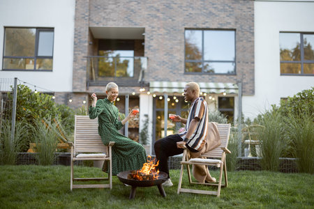 Multiracial couple drinking cocktails during home party in their garden. Burning fire for bbq....