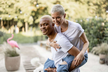 Latin boyfriend giving piggyback ride for his caucasian girlfriend on home terrace. Concept of relationship and enjoying time together. Modern domestic lifestyle. Warm sunny daytime.の写真素材