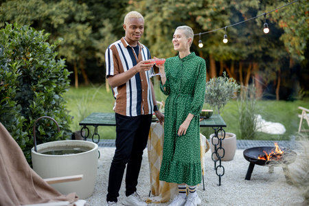 Multiracial couple hanging out together during a dinner at their backyard in the evening. Clinking...