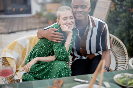 Latin man hugging his european girlfriend during a lunchtime in their garden. Joyful multiracial couple enjoying time together. Concept of relationship. Modern domestic lifestyleの写真素材