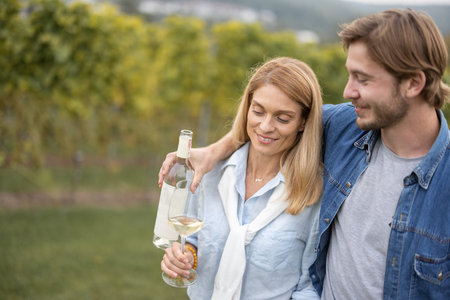 Happy european couple walking near vineyards in countryside. Man and woman drinking wine. Guy...