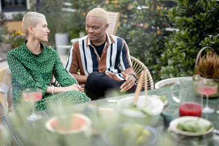 Multiracial couple talking and having fun during a dinnertime at their garden of country house. Idea...