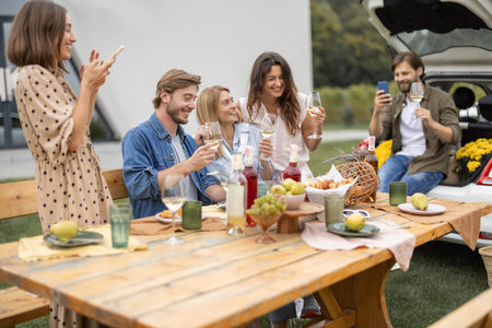Joyful european friends drinking toasting and having fun with local wine during picnic near...