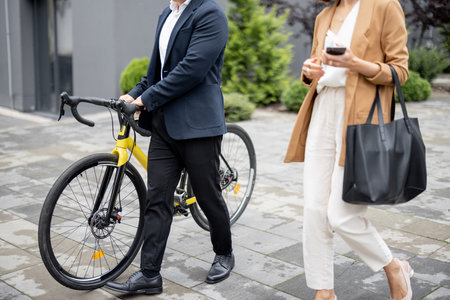 Asian businessman and caucasian businesswoman walking, drinking coffee and talking in city. Concept of business cooperation. Man with bicycle. cropped image with no faceの写真素材