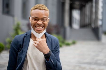 Young businessman taking off medical mask and enjoying fresh air on city street. Concept of health protection during Coronavirus pandemic. Pleased man wearing formal wearの写真素材