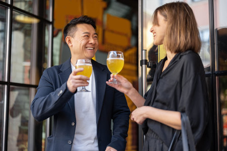 Caucasian woman and asian man drinking and toasting cocktails at cafe. Concept of relationship and...