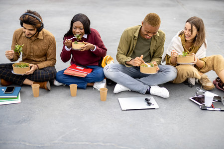 Multiracial students sitting and eating salad during lunch on asphalt at university campus. Concept...