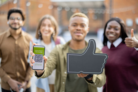 Multiracial students showing smartphone with app of Coronavirus Vaccination and thumb up gesture at...