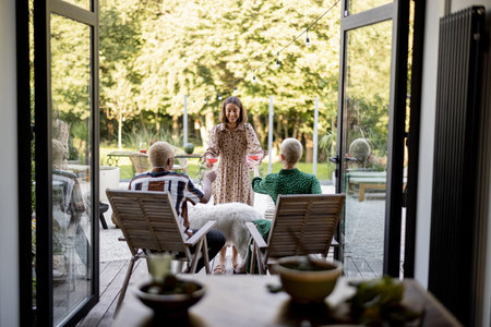 Woman giving cocktails to a friends sitting on wooden chairs at home terrace. European girls and...