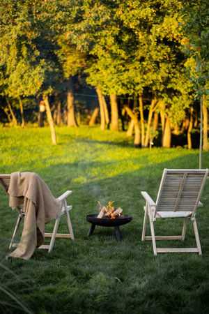 Two loungers with bonfire in bowl on a green lawn near the forest. Beautiful barbecue zone on nature.の写真素材