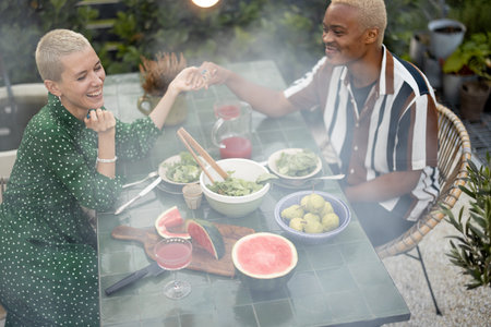 Multiracial couple having dinner at backyard of their country house on nature. Idea of healthy eating and modern lifestyle. Black man and european woman enjoying time togetherの写真素材