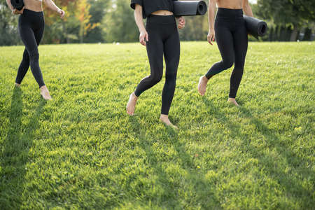 Cropped image of girlfriends with fitness mats on grass at sunny day. Concept of healthy lifestyle. Girls practicing yoga and doing sport exercices. Athletic women barefoot and wear sportswearの写真素材