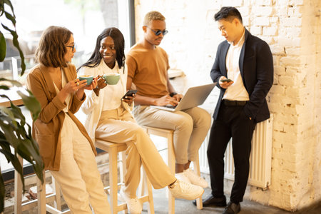 Multiracial business team having break during work in cafe or restaurant. Concept of rest on work. Women drinking tea and talking. Men using digital gadgets. Idea of business cooperationの写真素材