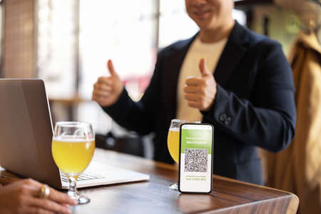 Cropped image of man showing OK sign with app of Coronavirus Vaccination green pass in cafe. Concept of health protection during pandemic. Idea of rest and leisureの写真素材