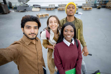 Group of multiracial students looking at camera on territory of university campus. Concept of education and learning. Idea of student lifestyle. Friendship. Black man with electric scooterの写真素材