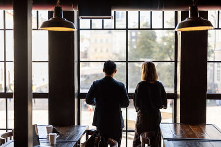 Side view of asian man and caucasian woman talking in cafe or coworking near window. Concept of relationship and spending time together. Idea of friendship. Modern loft interior at sunny dayの写真素材