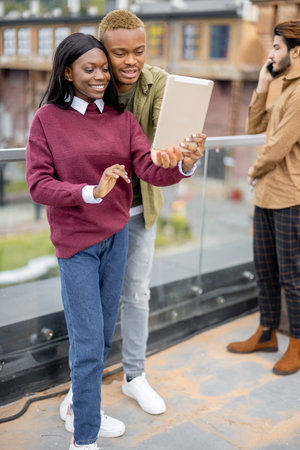 Black students having video call on digital tablet outdoors. Concept of remote and e-learning. Idea of students lifestyle. Smiling young girl and guy. Man waving hand. University campusの写真素材