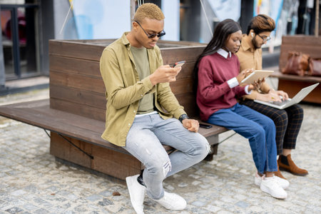 Multiracial students using gadgets outdoors. Concept of education. Remote and e-learning. Idea of...