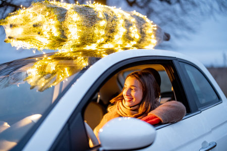 Happy woman driving car with a illuminated Christmas tree on a rooftop. Concept of New Year...