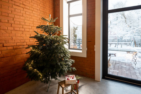 Cozy living room interior with Christmas tree in the corner. Concept of home comfort in winter. Windows overlooking a snowy garden, home with brick wallの写真素材