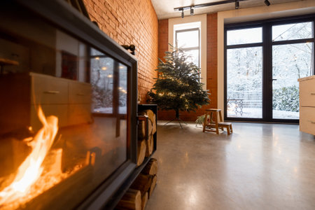 Cozy living room interior with Christmas tree and burning fireplace. Concept of home comfort in winter. Windows overlooking on snowy garden, room with brick wall and concrete floorの写真素材