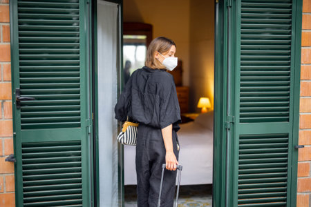 Woman in medical mask with baggage entering in hotel room. Concept of weekend, rest, tourism and...