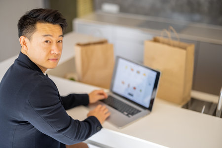 Man choosing groceries in online store on laptop computer on kitchen at home. Concept of online...