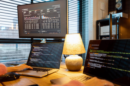 Female programmer writing programming code on laptops and desktop computer at cozy home workplace....