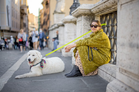 Woman with her white dog sitting on the street in Rome. Elegant woman in coat with italian shepherd...