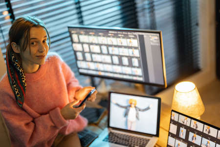 Portrait of a young creative woman work on laptop and desktop computers editing photos at cozy home office. Portrait of female photographer at home workplaceの写真素材
