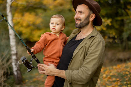 Smiling caucasian man fishing with little son on river or lake coast. Concept of leisure and weekend in nature. Family relationship and spending time together. Warm autumn dayの写真素材