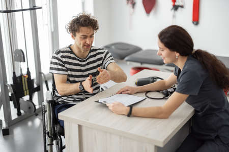 Medical worker talking with a young man in a wheelchair before training in the rehabilitation center. Concept of medical care and support for people with injuriesの写真素材