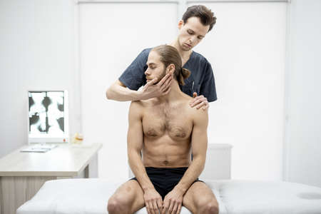 Physical therapist does manual therapy to a young athletic guy at medical office. Concept of manual therapy and osteopathyの写真素材