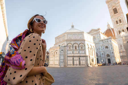 Woman enjoys beautiful view on famous Duomo cathedral in Florence, standing on empty cathedral square during morning time. Stylish woman visiting italian landmarks. Traveling Italy conceptの写真素材