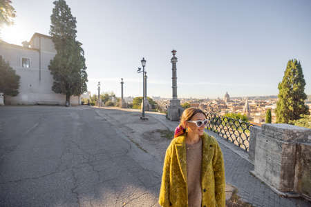 Woman enjoying beautiful morning cityscape of Rome, walking in Villa Borghese Park. Old fashioned woman wearing coat with colorful shawl in hair. Concept of italian lifestyle and travelの写真素材