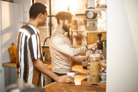 Two guys of different ethnicity having warm conversation while making coffee on kitchen at home. Concept of close male friendship or relationship as gay couple. Caucasian and hispanic man togetherの写真素材