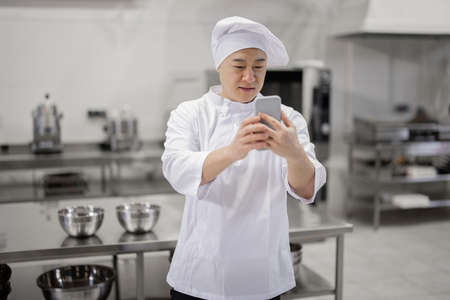 Asian chef with phone in the professional kitchenの写真素材