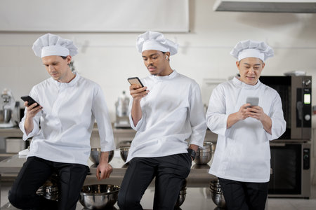 Multiracial team of chef cooks with phones during a break at restaurant kitchen