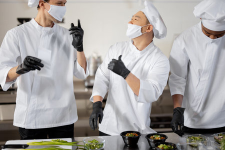 Chefs in face masks prepare takeaway food in professional kitchenの写真素材