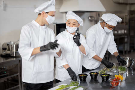 Chefs in face masks prepare takeaway food in professional kitchenの写真素材