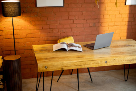 Stylish and cozy workplace with a wooden table and floor lamp on brick wall background at home....